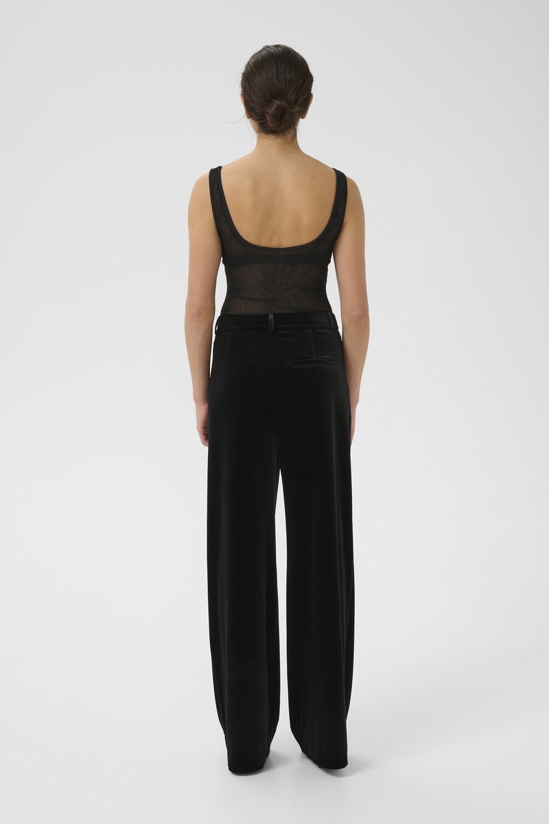 Black sleeveless bodysuit with a sheer texture and low back; paired with wide-leg black pants in soft fabric featuring a back pocket.