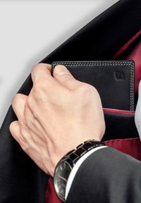 Black leather wallet with white stitching, partially inserted into a suit jacket's inner pocket, against a red silk lining. Hand gripping wallet.