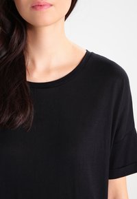 Czarny, krótki rękaw t-shirt z okrągłym dekoltem, wykonany z miękkiego, lekkiego materiału. Gładka tekstura bez widocznych wzorów czy akcentów.