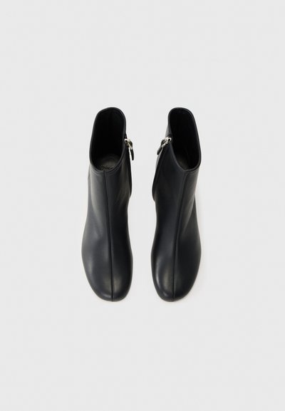Musta nahka nilkkaboots, joissa on sileä rakenne, sivu vetoketjukiinnitys ja tyylikäs, minimalistinen muotoilu.