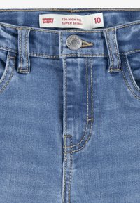 Jeans Levi's 720 de talle alto super ajustados en denim azul claro. Presentan un cierre de botón, trabillas para cinturón y costuras en contraste. La etiqueta de tamaño indica 10.