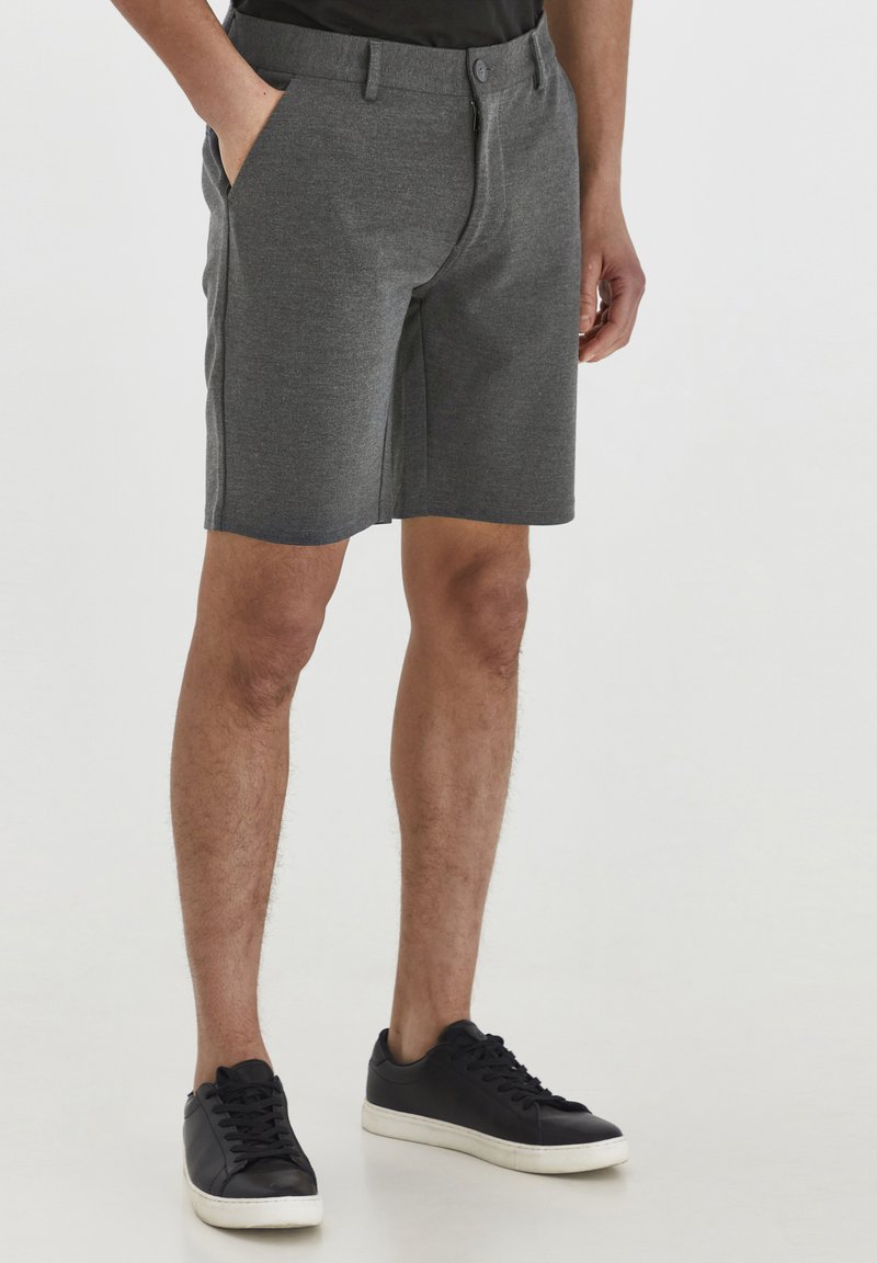 Gray, knee-length shorts with side pockets and a structured waistband. Paired with black sneakers, featuring a smooth leather finish.