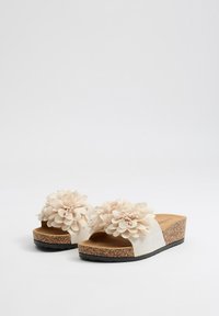 Sandalias de plataforma beige con suela de corcho, que cuentan con grandes acentos de flores de tela en las correas y una textura suave en la parte superior.