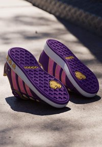 Fioletowo-różowy sneaker z teksturowaną gumową podeszwą, ozdobiony złotymi detalami i wzorzystym motywem.