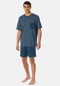 Marineblaue kurzärmlige Hemd mit weißem Karomuster und Tasche, kombiniert mit einfarbigen marineblauen Shorts, aus weichem Baumwollstoff hergestellt.