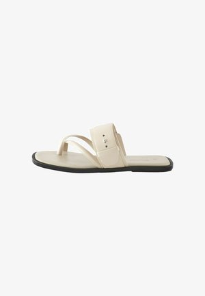 Beige flat sandal with two crossed straps and a side strap, crafted from smooth material, featuring a minimal design and black sole.