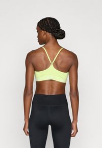 Αθλητικό σουτιέν Nike σε έντονο κίτρινο χρώμα με ρυθμιζόμενες τιράντες, διαθέτει φαρδιά λευκή ταινία με λογότυπο. Λείο ύφασμα και σχεδιασμός racerback.