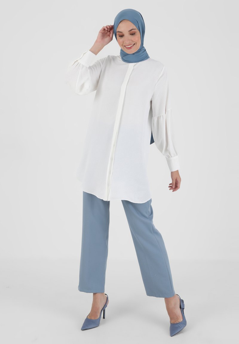 White long-sleeve blouse with button front and gathered sleeves, paired with light blue wide-leg trousers and light blue heels.