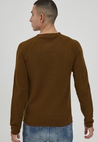Brown textured long-sleeve top with a round neckline and raglan sleeves, worn by a person from the back against a plain background.
