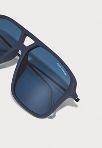 Ochelari de soare din plastic de culoare bleu marin, cu lentile mari pătrate și sticlă tăiată în nuanță de albastru închis. Marcați cu 'Armani Exchange' pe lentilă.
