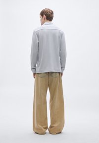 Ανοιχτό γκρι μακρυμάνικη μπλούζα με γιακά, συνδυασμένη με φαρδιά μπεζ παντελόνια από κορδούρα. Ομαλή υφή, χαλαρή εφαρμογή και εμφανείς ραφές.