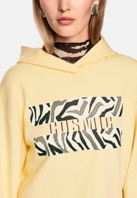 Yellow hoodie featuring a graphic with black and white zebra patterns and the word "COSMIC" in beige across the chest area.