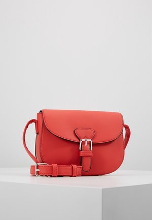 Red leather crossbody bag with a flap and a buckle closure. Features a textured finish and an adjustable strap. Compact and round shape.