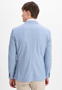 Helles blauer Blazer mit strukturiertem Design, texturiertem Stoff, Schventil, und schwarzen Knopfakzenten. Die Rückansicht zeigt eine taillierte Passform und minimalistische Linien.