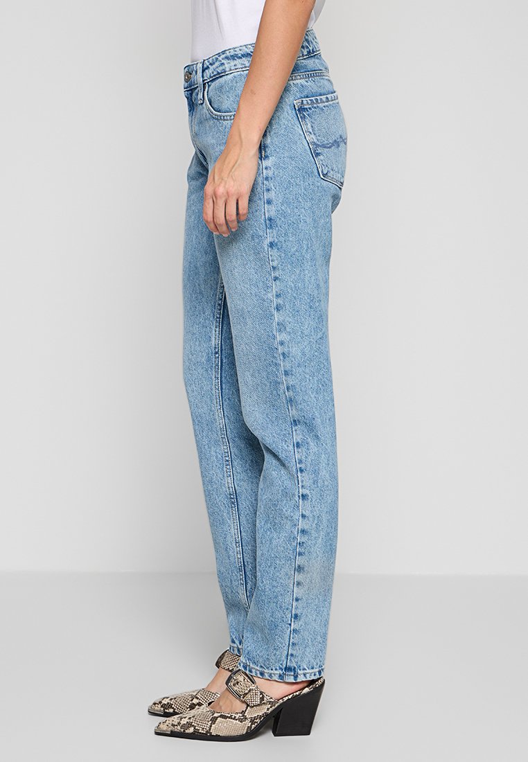 Jeans taille haute bleu clair avec une coupe droite, présentés avec un style classique à cinq poches et une légère décoloration. Complétés par des talons à motifs.