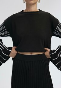 Black knitted crop top with striped long sleeves paired with a pleated black skirt, highlighting texture and form.