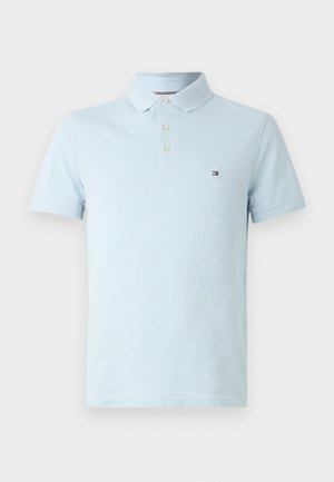 Polo shirt bleu clair en tissu texturé, avec un col classique, trois boutons et un petit logo sur le côté gauche de la poitrine.