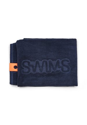 Serviette bleu marine pliée avec « SWIMS » embossé en grandes lettres, étiquette orange sur le côté gauche, fond blanc uni.