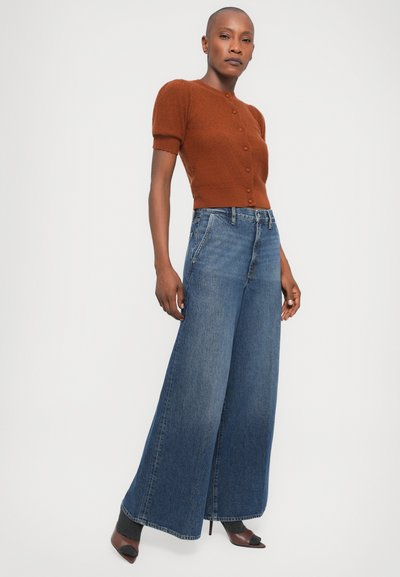 Brown knit cardigan with short sleeves and button front, paired with wide-leg blue jeans. The jeans feature a high waist and subtle fading.