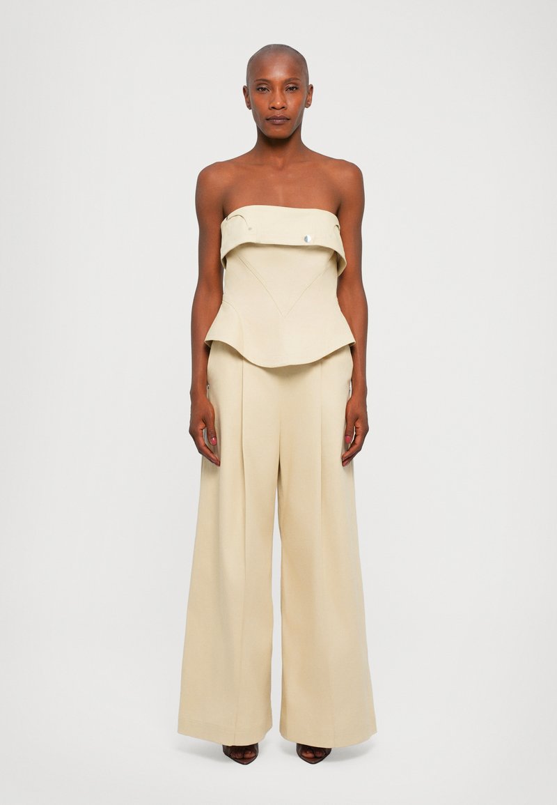 Top bege sem alças com silhueta peplum, combinado com calças largas. Textura suave, hardware mínimo, exibindo um design sob medida.