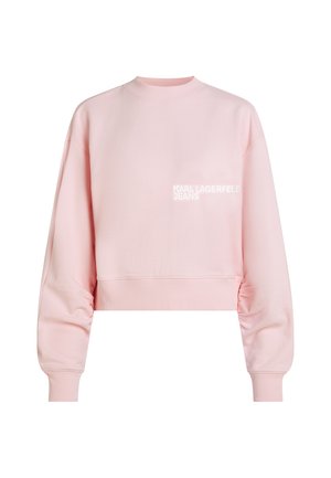 Svjetloružičasta skraćena majica s dugim rukavima i rebrastim manžetnama, s malim bijelim natpisom "KARL LAGERFELD JEANS" na prsima.