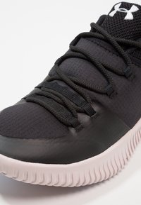 Black athletic shoe with a textured fabric upper, black laces, and a white rubber sole featuring vertical grooves. Logo on the tongue.