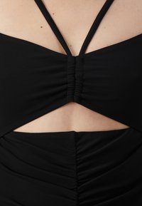 Vestido negro con fruncidos, que presenta un diseño recortado en la cintura y tirantes finos. La textura es suave, resaltando la silueta ceñida.