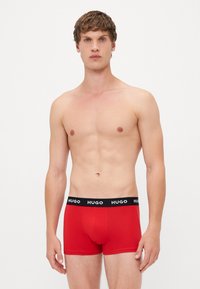 Rote Baumwoll-Boxershorts mit einem schwarzen Bund, der das "HUGO"-Logo trägt, entworfen für eine enge Passform und mittlere Bedeckung.