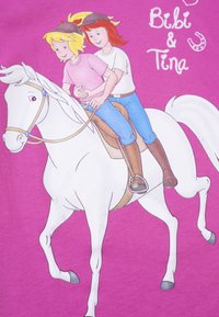 Rosa Textilie mit zwei animierten Charakteren, die auf einem weißen Pferd reiten. Die Charaktere tragen Helme und lässige Reitbekleidung, mit einem schlichten Hintergrund.