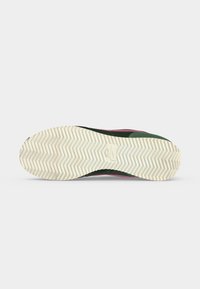 Rubber sole of a dark green and pink athletic shoe with herringbone tread pattern and a small rectangular logo in the center.