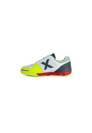 Zapatilla deportiva blanca con parte superior de malla, acentos amarillos, suela gris y roja, con un destacado logo 'X' negro en el lateral.