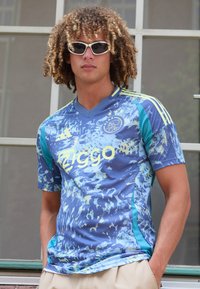 Maglia da calcio dell'Ajax con un motivo astratto blu e turchese, maniche corte, e logo con il testo "Ziggo" in giallo brillante.