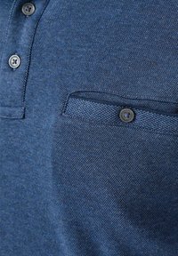 Blaues geprägtes Poloshirt-Gewebe mit einer kleinen Knopftasche und zwei dunklen Knöpfen in der Nähe des Kragens.
