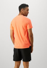 Kortermet t-skjorte i lys orange med vertikale striper og rund hals, kombinert med svarte shorts. Glatt tekstur.
