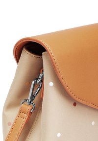 Kožený klapka v tan barvě pokrývá béžovou tašku z látky s malými puntíky. Obsahuje kovové komponenty a klip pro připevnění popruhu.