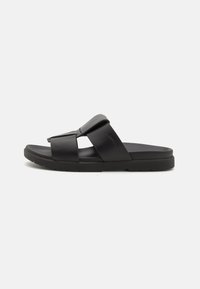 Svarte sandaler i plast med bred stropp og strukturert fotseng; flat såle med litt grepdetalj.