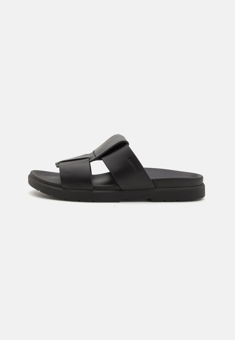 Zwarte slide sandalen van synthetisch materiaal; voorzien van een brede band en een gestructureerde voetbed; vlakke zool met een lichte grip detail.