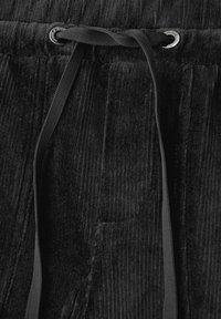 Pantaloni di velluto a coste neri con un cordoncino nero infilato attraverso occhielli in metallo argentato nella cintura elastica.