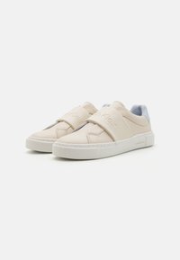 Calvin Klein sneakers i beige syntetisk materiale, med en slip-on design som har brede stropper og hvite gummisåler. Lys blå detaljer bak.