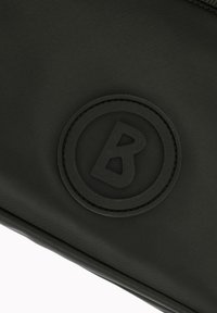 Črna najlon torbica z teksturiranim okroglim gumijastim logotipom s črko 'B' v središču, elegantna zasnova in gladka površina.