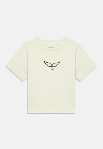 Cremefarbenes T-Shirt mit kurzen Ärmeln, schwarzen Flügelmotiv und der Aufschrift "1997" unter dem Motiv auf der Brust.