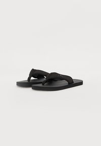 Flip-flops negre cu o talpă din cauciuc texturat și o curea moale și netedă. Au un logo pe curea, concepute pentru purtare casuală.