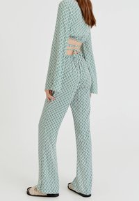 Uppblåsta byxor och långärmad topp i grön och vit mönster, med utskuren ryggdetalj och knytband. Tillverkad av lättviktig tyg.