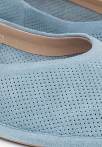 Jasnoniebieskie zamszowe buty wsuwane z perforowanymi detalami i gładkim beżowym wykończeniem wzdłuż otworu. Miękka faktura i okrągły kształt.