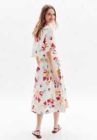 Abito floreale realizzato in tessuto leggero, caratterizzato da maniche corte, una forma fluida e una base bianca con motivi floreali colorati. Sandali marroni.