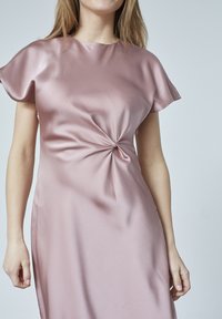 Satin rosa klänning med rund hals, korta fjäderlätta ärmar och en framåtvänd twistdetalj vid midjan. Slät textur och flödande design.