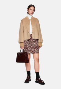 Beige wool blend jacket, white turtleneck, burgundy floral skirt, dark socks, glossy burgundy handbag, and chunky black shoes with hardware detail.