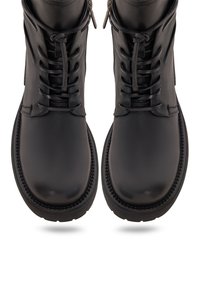 Botas de cuero negro con cordones, puntera redonda, suelas gruesas y cremalleras laterales, vistas desde arriba sobre un fondo blanco.