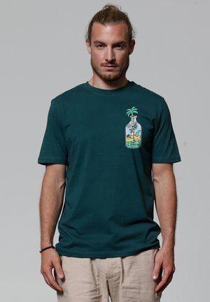Dark green cotton t-shirt with short sleeves and a front pocket graphic of a tropical scene inside a bottle. Smooth texture.
