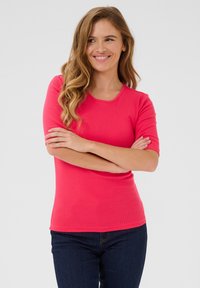 Tight sittande t-shirt med kort ärm i livfull rosa, ribbat mönster, rund halsringning. I kombination med mörkblå denim står modellen med armarna i kors.